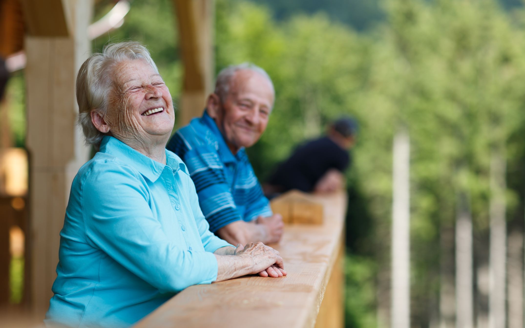 An elderly couple look out over their balcony at the woods