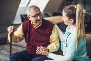 A nurse holds a man hand as they talk comfortably together