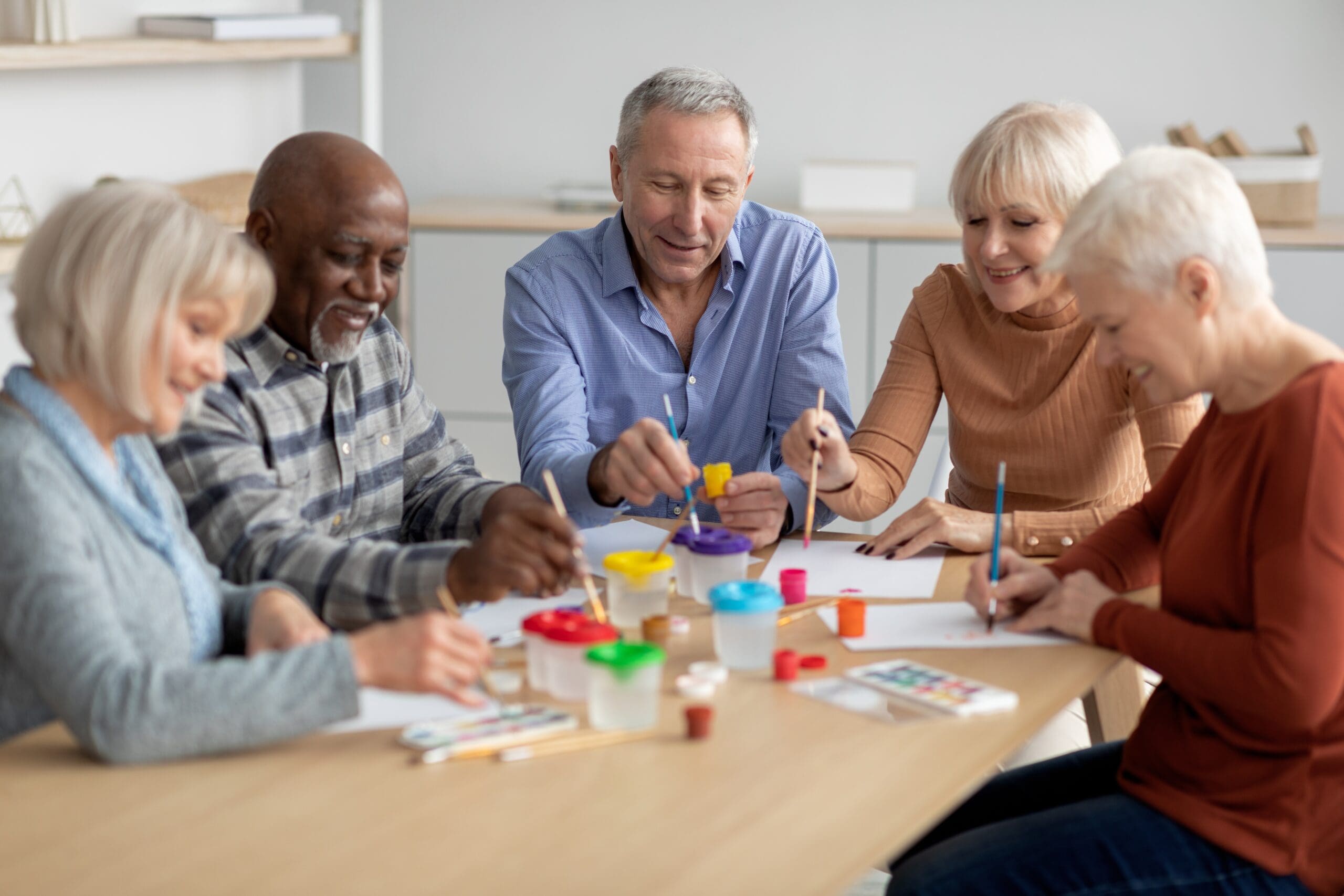 A group of older people paint together at a table