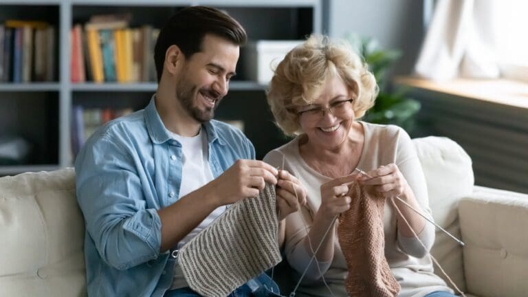 A smiling man and oldeer woman enjoy learning to crochet together