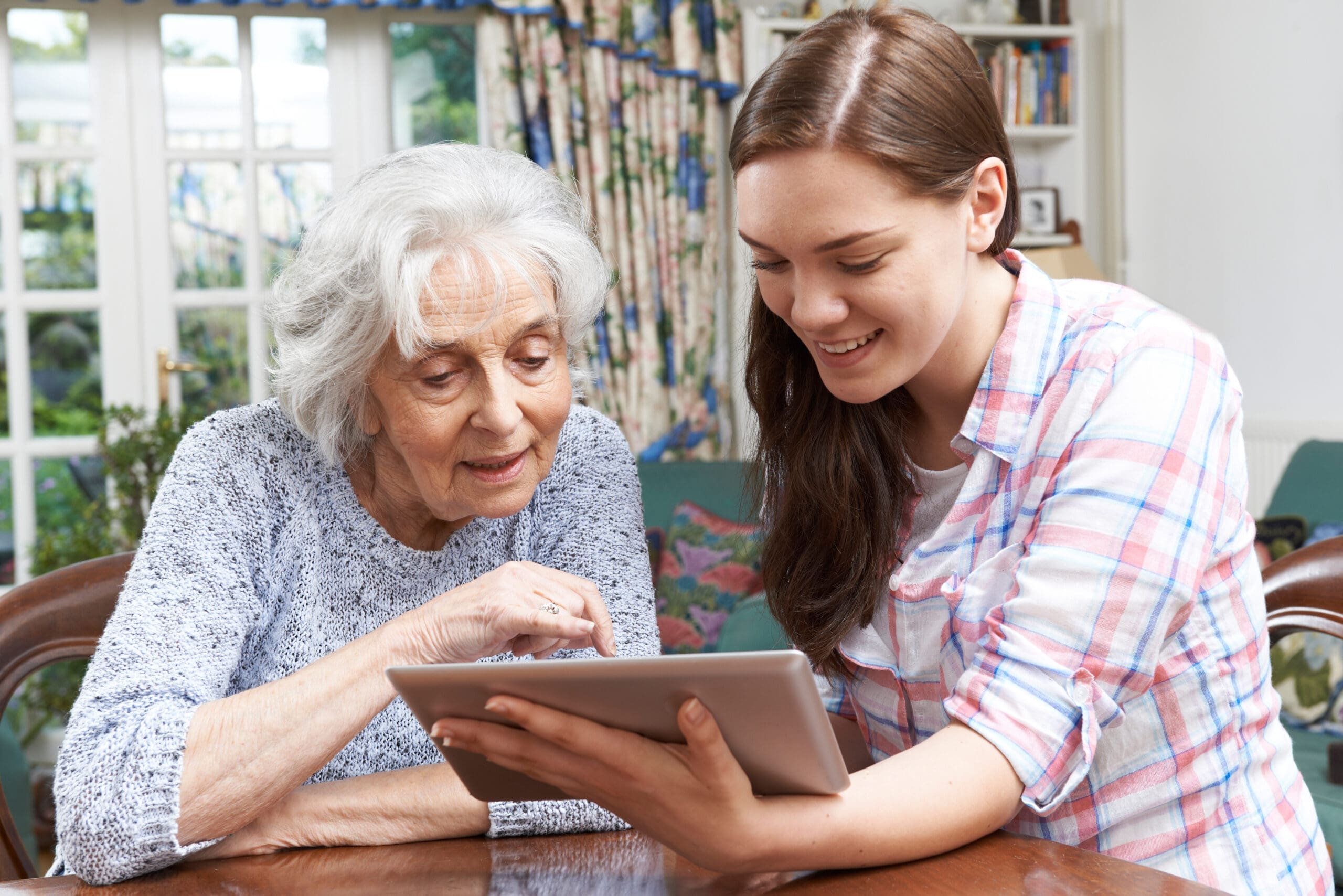 An older woman looks at a tablet with her carer