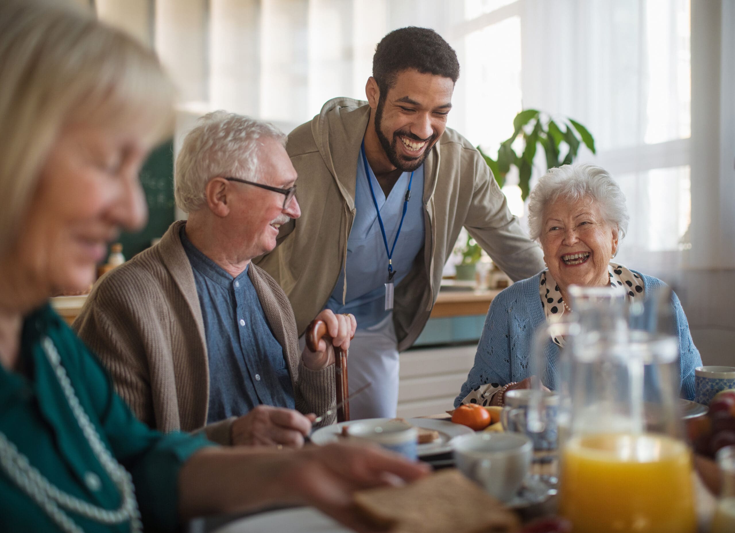 A male carer laughs with two older women and a man at the breakfast table