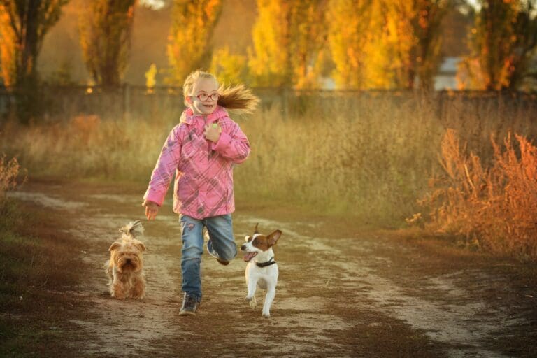 A little girl with Down's Syndrome runs in the autumn sun accompanied by her two small dogs