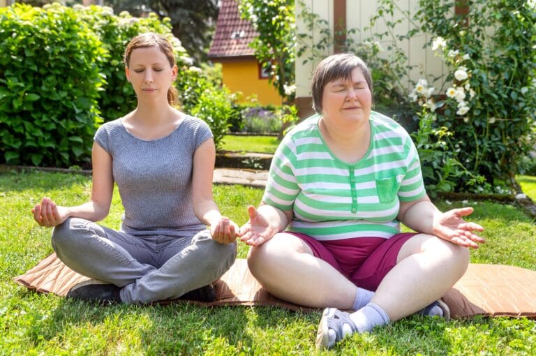 Two women - one a carer and one a person being supported - practice yoga outside in the sunshine