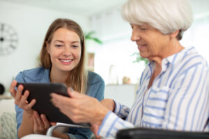 A woman and an older lady look at an electronic tablet together