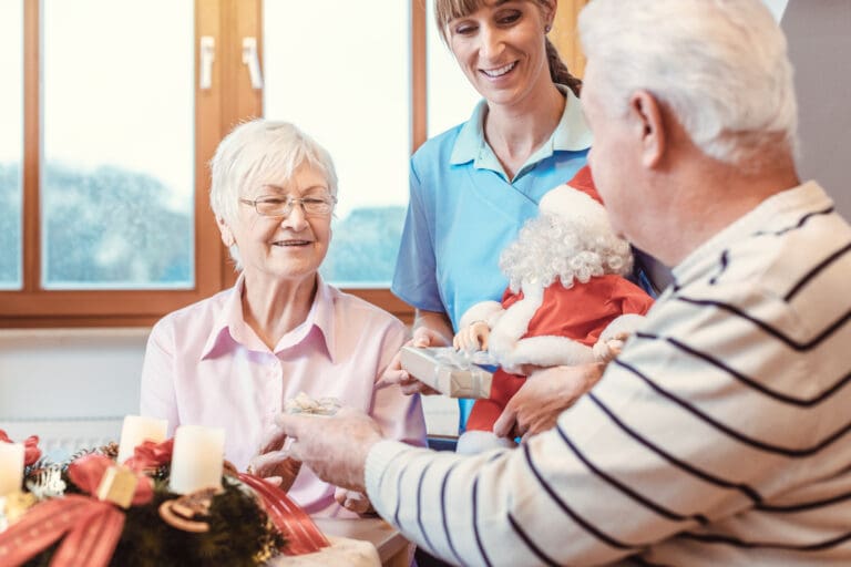 A care worker hands an elderly couple a holiday gift