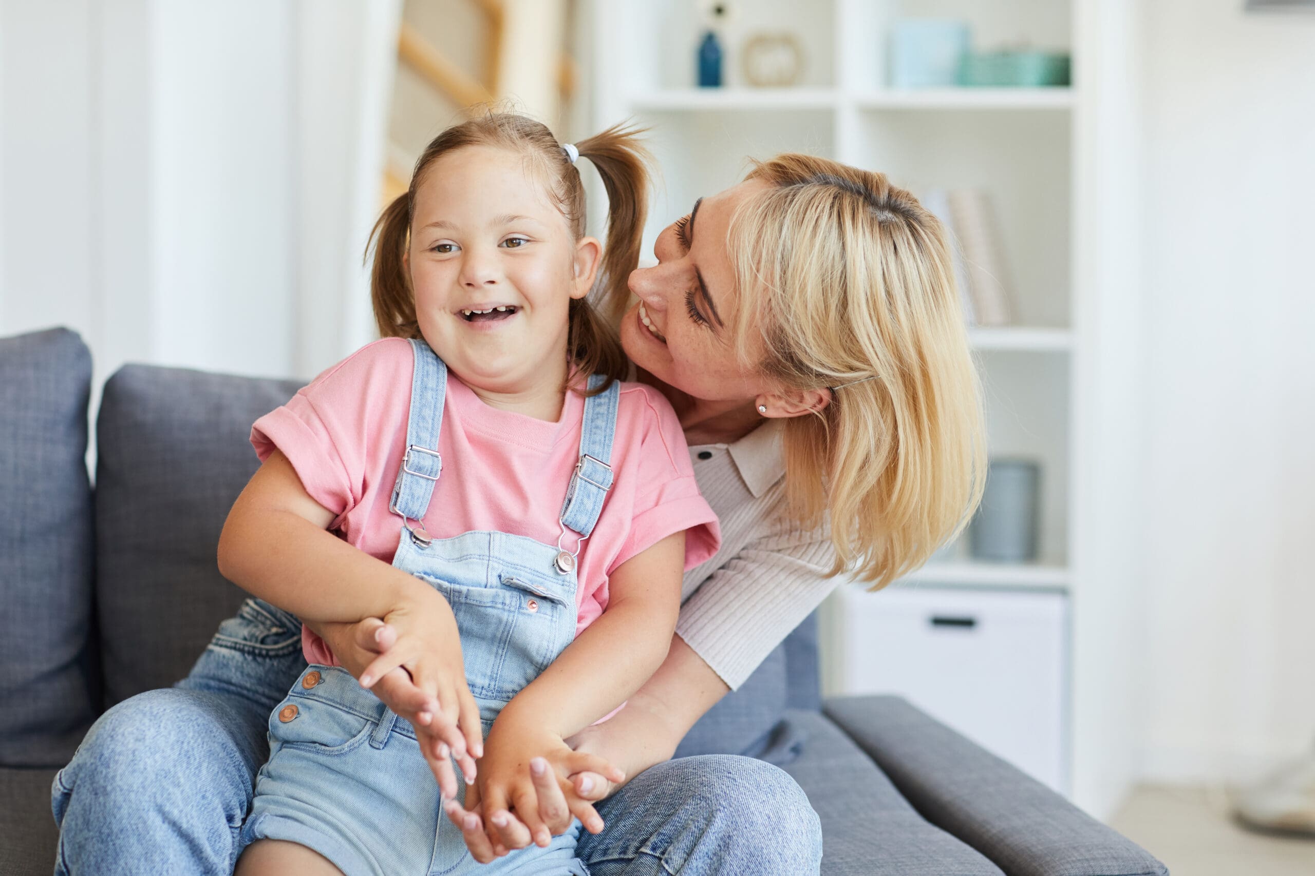 A woman embraces her young daughter whilst sat on the sofa