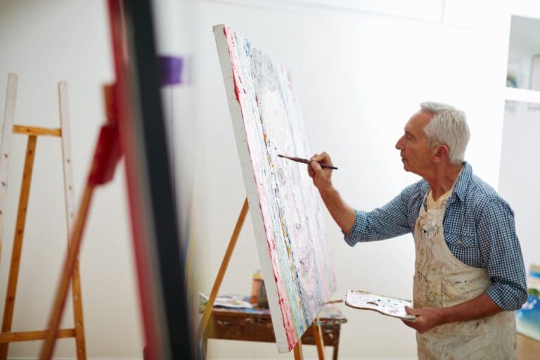 An older man concentrates on painting at an easel