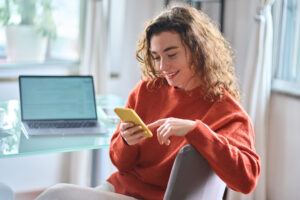 A woman looks at her phone and smiles whilst at her desk working