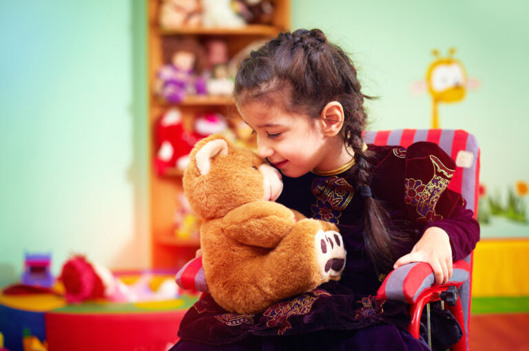 A little girl in a wheelchair hugs her teddybear