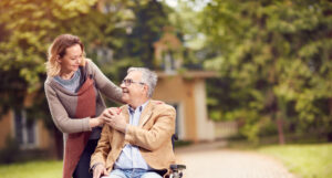 An older gentleman and a woman hold hands whilst outside in nice weather