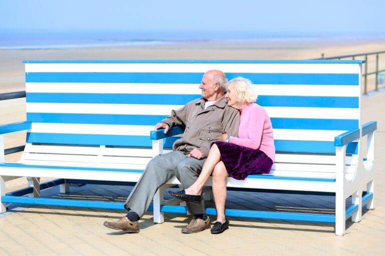 A happy senior couple relax on the beach sitting together on the bench