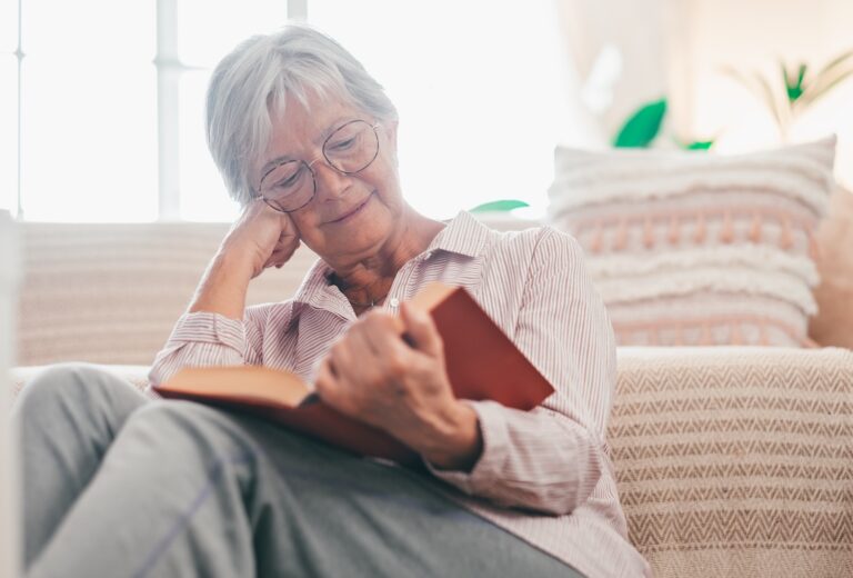 Portrait of relaxed senior woman sitting on the floor at home while reading a book enjoying free time